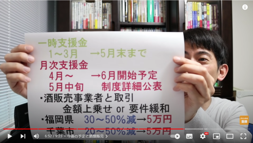 山田さんが支援金の今後について解説している場面。手には、支援金の今後が書かれた紙を持っている。