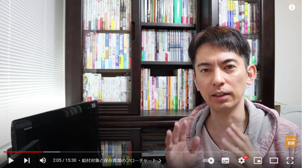 山田さんが支援金の対象者かどうか解説をし始める場面。山田さんは本棚の前に座っている。