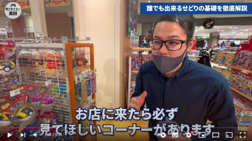 高田さんはイオンの玩具コーナーに来ています。
画面下には｢お店に来たらかならず見てほしいコーナーがあります｣と高田さんが話されている言葉の字幕が設置されています。
高田さんはこの場面で、ショーケースに飾ってあるおもちゃについて解説しようとしています。